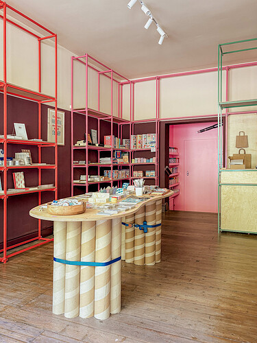 The interior of The Stationer, with colourful metal shelving, a central display table made of large cardboard tubes, and various stationery items.